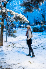 Photo of a young and attractive woman with short hair walking through the snow wearing winter clothes. Blue sky during the night. Magical landscape