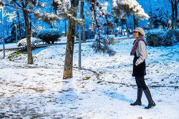 Photo of a young and attractive woman with short hair walking through the snow wearing winter clothes. Blue sky during the night. Magical landscape