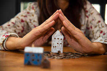 Closeup image of a woman collecting and putting coins in a glass jar with wooden house models.saving money concept