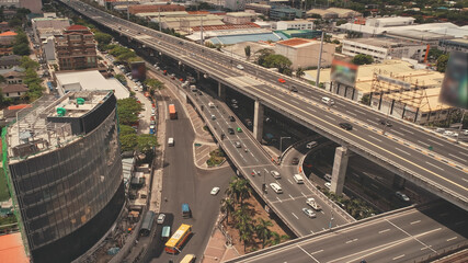 Fototapeta premium Manila cityscape at road with cars, trucks. Modern buildings aerial view. Amazing city scape with cottages, skyscrapers of traffic roadway. Cinematic drone shot of Philippines capital town
