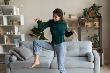 Overjoyed millennial Caucasian female renter have fun dancing in cozy living room on lazy leisure weekend. Happy young woman celebrate relocation moving to new own home or apartment. Rental concept.