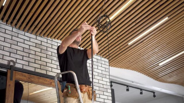 An electrician installs low-voltage LED lights on a plank ceiling. Service for replacing lamps and repairing electrical wiring. Modern wood plank ceiling design for a loft-style interior.