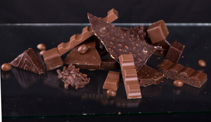 Broken chocolate pieces and cocoa powder on wooden background.