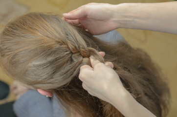 A woman braids a pigtail for a red-haired girl. Hair weaving hairstyles. Braiding close up