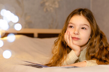 A child, 7-year-old girl with long blonde hair reading a children's book while lying on the couch....