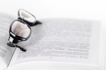Open pages book and glasses lying on it isolated on white background macro