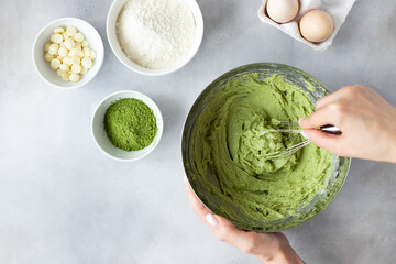 female hands mixing dough with whisk and recipe ingredients on gray background. Making Matcha Green...