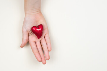 Small red heart in a female hand on a beige background, place for text