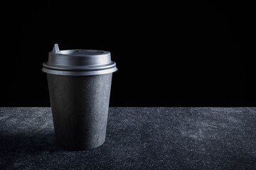 Black paper disposable takeout drink cup on dark surface and black background