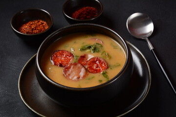 Caldo Verde Soup with greens and chopped chorizo on the top in the bowl on a dark background.