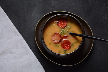 Caldo Verde Soup with greens and chopped chorizo on the top in the bowl on a dark background.