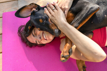 Young beautiful woman is engaged in gymnastics in the park with a doberman dog