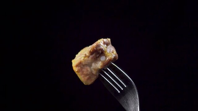 Pork fried with turmeric close up on a fork on a black background