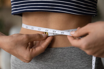 Crop close up of woman hold measurement tape measure waist after dieting training or going for sports. Fit female care about body shape, follow healthy lifestyle. Wellness, weight loss concept.