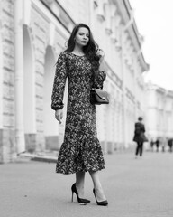 Fototapeta premium Elegant woman in dress walking city street on fall or autumn day. Pretty girl with long wavy hair holding handbag