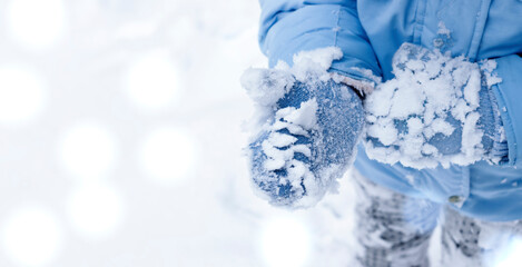 The baby is playing with the snow. Blue mittens and a blue jacket in the snow. Copyspace