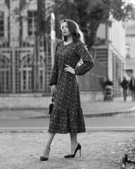 Elegant woman in purple dress walking city street on fall or autumn day. Pretty girl with long wavy hair holding handbag