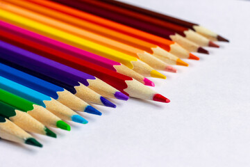 Colored pencils lying in a row on a sheet of white paper.