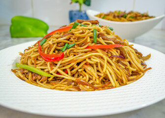 Closeup of beautifully arranged Chicken Noodles garnished with red and green bell peppers and spring onions