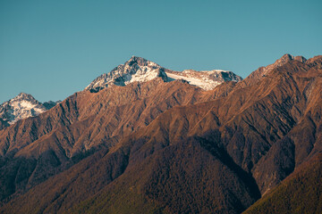 Beautiful brown mountains with snow-capped peaks against a blue sky. Natural wallpaper.