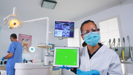 Patient pov of dentist explaining dental radiography and diagnosis for teeth infection using tablet with green screen. Stomatology specialist pointing at mockup, copy space, chroma display