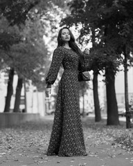 Elegant caucasian brunette woman with long wavy hair in long brown dress with floral print walking...