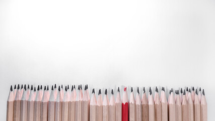 many simple pencils in a row on a white sheet, and among them a red pencil