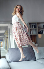 Smiling female model, jump on the couch with bare feet, looking at camera. Studio photo.