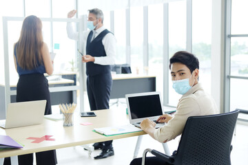 Fototapeta na wymiar Caucasian boss and Asian teamwork is wearing mask for preventing covid19 virus and brainstorming in meeting room at office. Healthcare and New normal lifestyle in business concept. Focus at asian man.