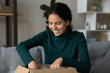 Excited millennial Caucasian woman unpack cardboard box shopping online on internet from home. Happy young female buyer have fun unboxing package with order buying on web. Delivery concept.