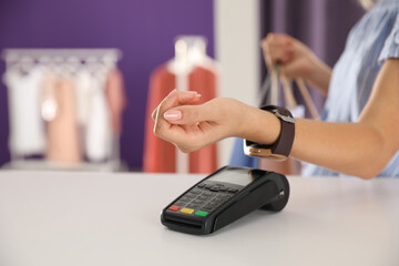 Woman using terminal for contactless payment with smart watch in shop, closeup