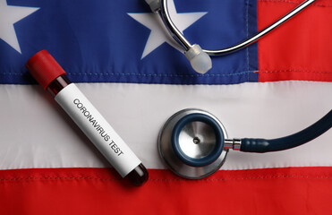 Test tube with blood sample and stethoscope on American flag, flat lay. Coronavirus pandemic in USA