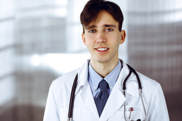 Friendly young male doctor standing with clipboard in modern clinic. Medicine concept