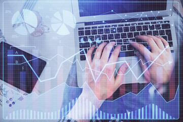 Double exposure of man's hands typing over laptop keyboard and forex chart hologram drawing. Top view. Financial markets concept.