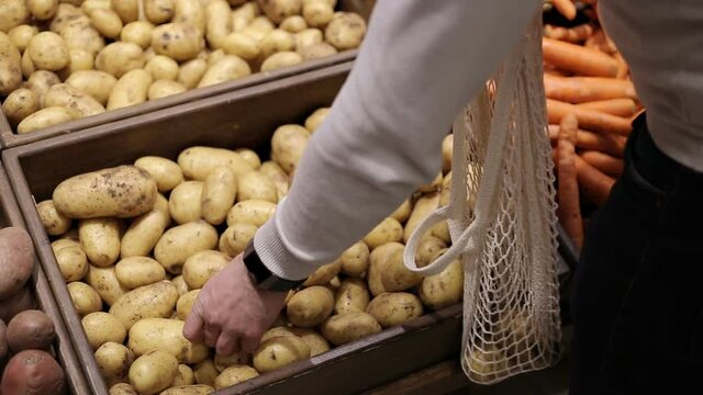 Close up of man hands puts potatoes into eco string bag at supermarket