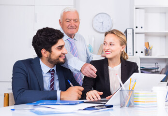 Employees are demonstrating reports on laptop to mature boss in the office.