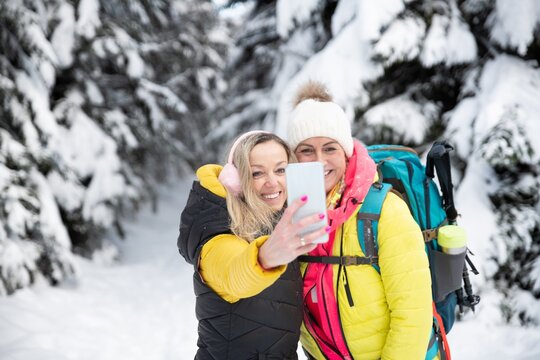 Two smiling friends are taking a picture of themselves in the mountains on the trail. Lovely winter scenery.