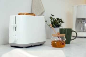 Modern toaster with bread slices and honey on white table in kitchen