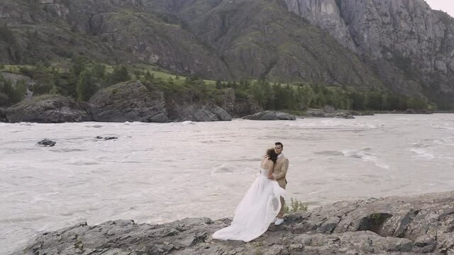 Bride and groom in a wedding dress on the river bank against the background of mountains in Altai