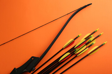 Black bow and set of arrows on orange background, flat lay. Archery sports equipment