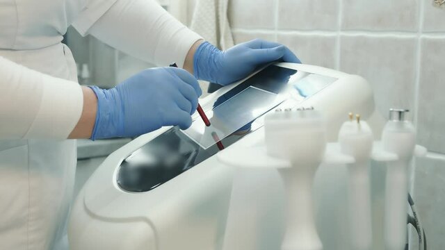 hand close up pressing a stylus on the touch screen of an innovative device for skin rejuvenation in a beauty salon