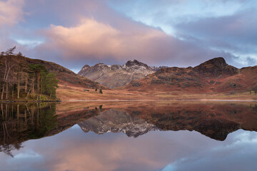 Beautiful vibrant Winter sunrise over Blea Tarn in Lake District with snow capped Langdale Pikes in distance