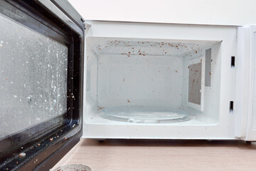 A dirty microwave oven with an open door in need of washing and cleaning. Hygiene problems and cleaning of kitchen appliances