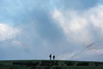 Epic landscape image of Skiddaw snow capped mountain range in Lake District in Winter with low level cloud around peaks viewed from Derwentwater
