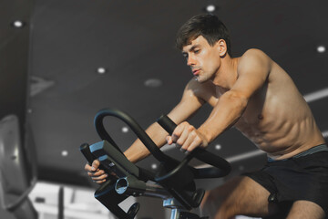 Fototapeta na wymiar Handsome caucasian athlete muscular male exercise on spinning bike at fitness gym