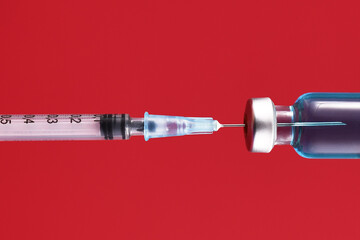 Syringe drawing up blue liquid from medical vial on red background