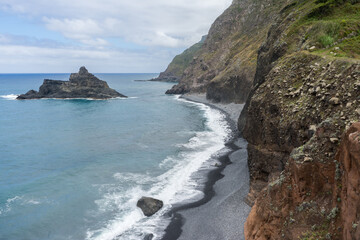 Fototapeta na wymiar Viewpoint at waves crashing onto black stone beach with tall mountains falling into the sea