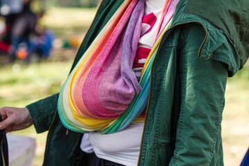 A baby sucks his mother's breast in nature wrapped in a sling scarf.