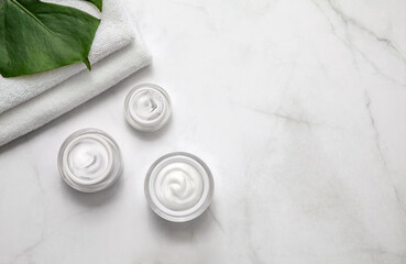 Moisturizing cream container jars with towel and monstera leaf on marble background. Flat lay, top...