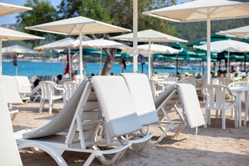 White sun loungers with mattresses and parasols stand on the tropical beach